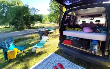 Volkswagen Caddy camper van with a camping box, rear hatch open at a campsite